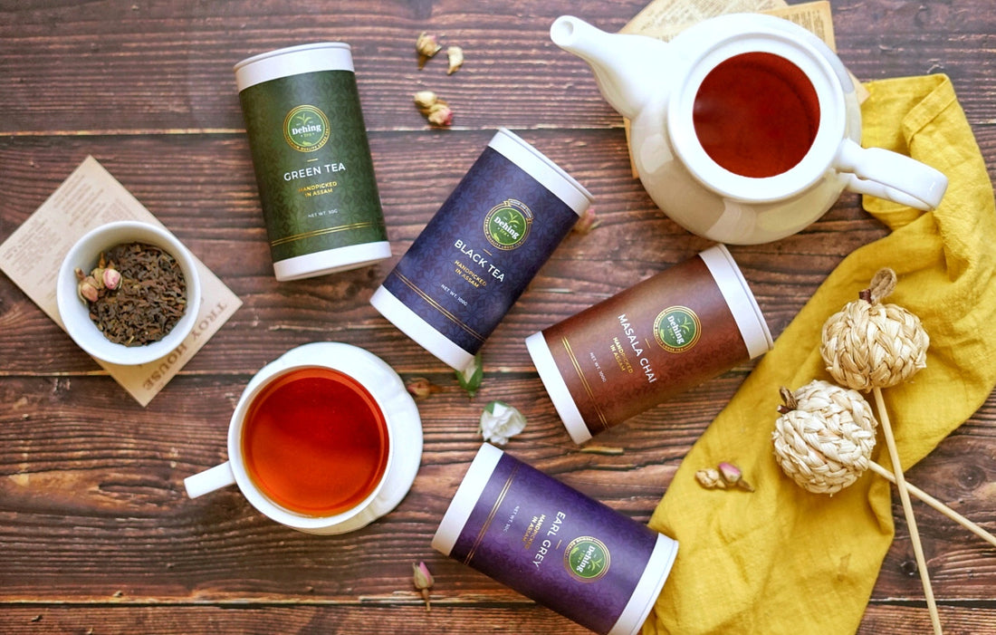 Dehing Assam Tea | Birds eye shot of different coloured tea caddys on a wooden table with a brewed cup of tea and open tea pot