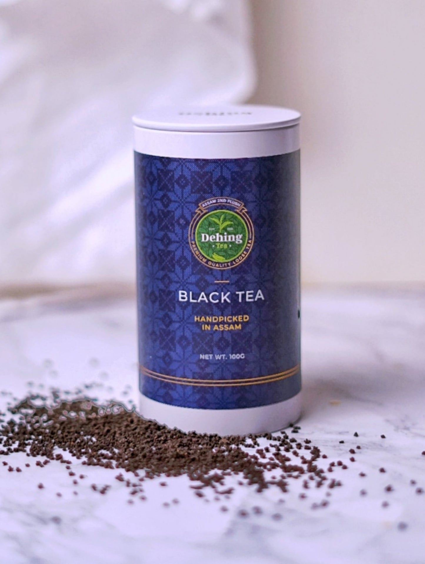 A Dehing branded tea caddy stating Black Tea and 2nd Flush Loose Tea on the packaging and showing the black tea scattered on the surface by the base of the gift caddy