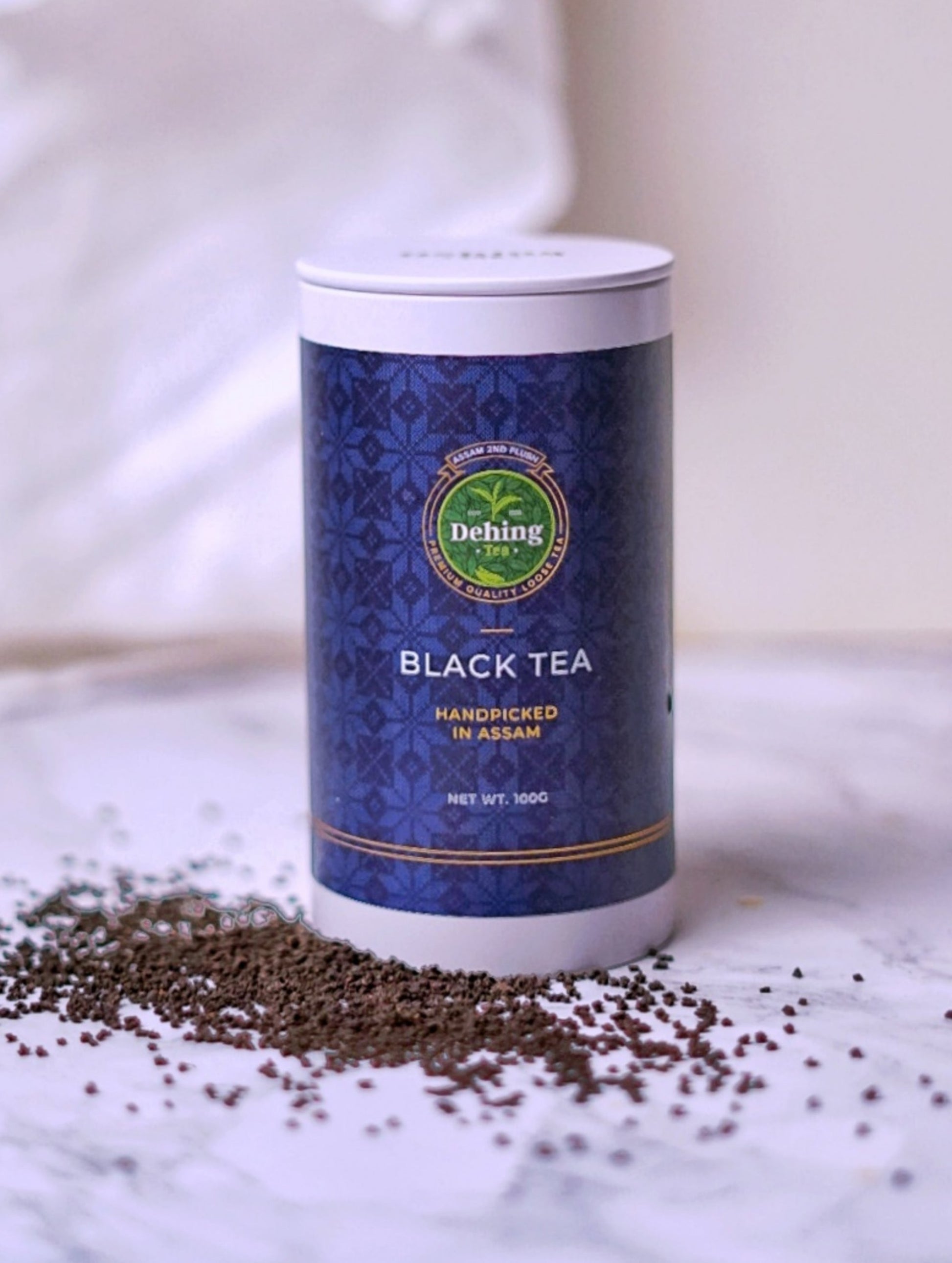 A Dehing branded tea caddy stating Black Tea and 2nd Flush Loose Tea on the packaging and showing the black tea scattered on the surface by the base of the gift caddy