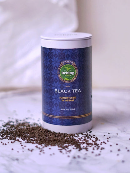 A Dehing branded tea caddy stating Black Tea and 2nd Flush Loose Tea on the packaging and showing the black tea scattered on the surface by the base of the gift caddy