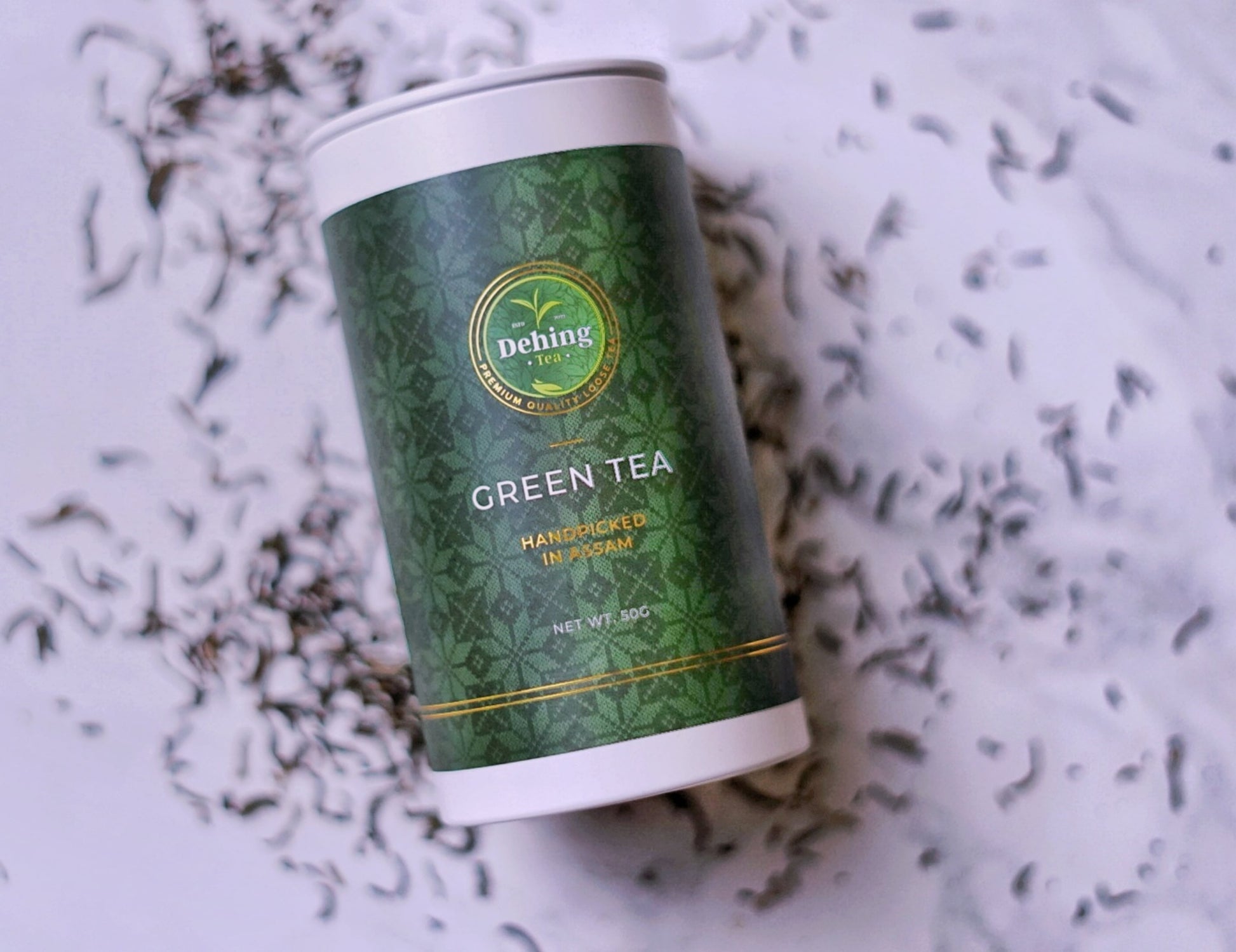 Assam green tea gift caddy canister with Dehing Tea logo on a white background with tea leaves.