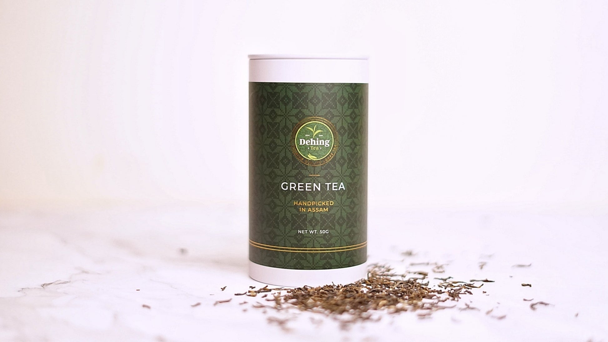Dehing tea caddy labelled 'Green Tea' with scattered tea leaves on a light background