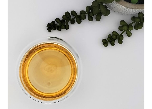 Glass of pure green tea on a white surface with green leaves