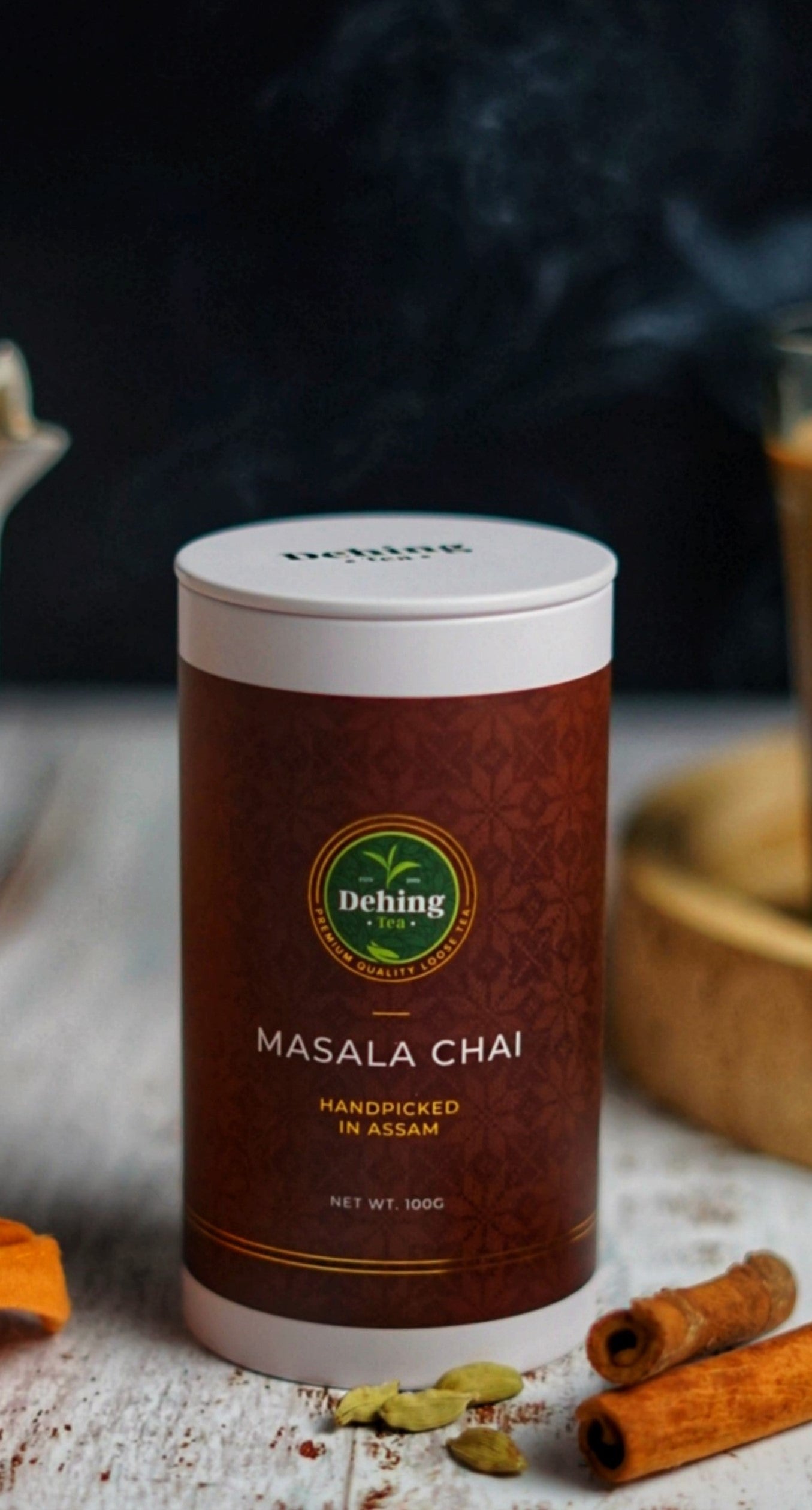 Dehing Masala Chai tea gift caddy on a rustic background with cinnamon sticks and cardamom and spices.