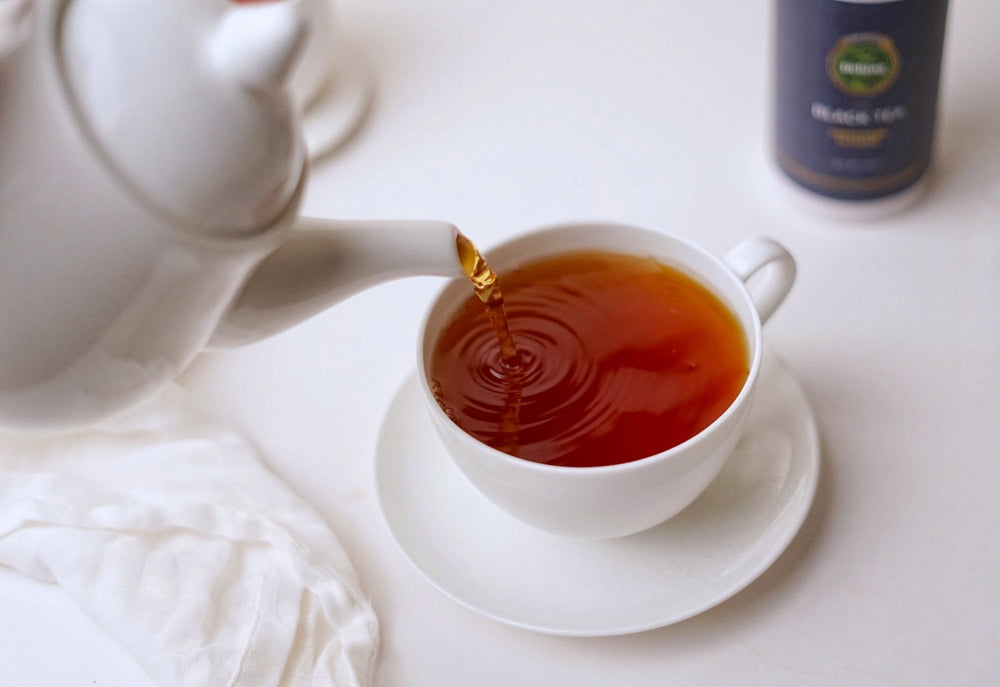 White tea pot pouring freshly brewed Assam black tea into white tea cup